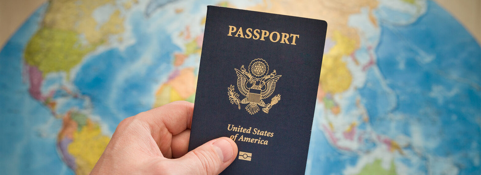 Hand Holding a US passport with us global in the back ground. Get Expedited Passport Services in {city}, {state}